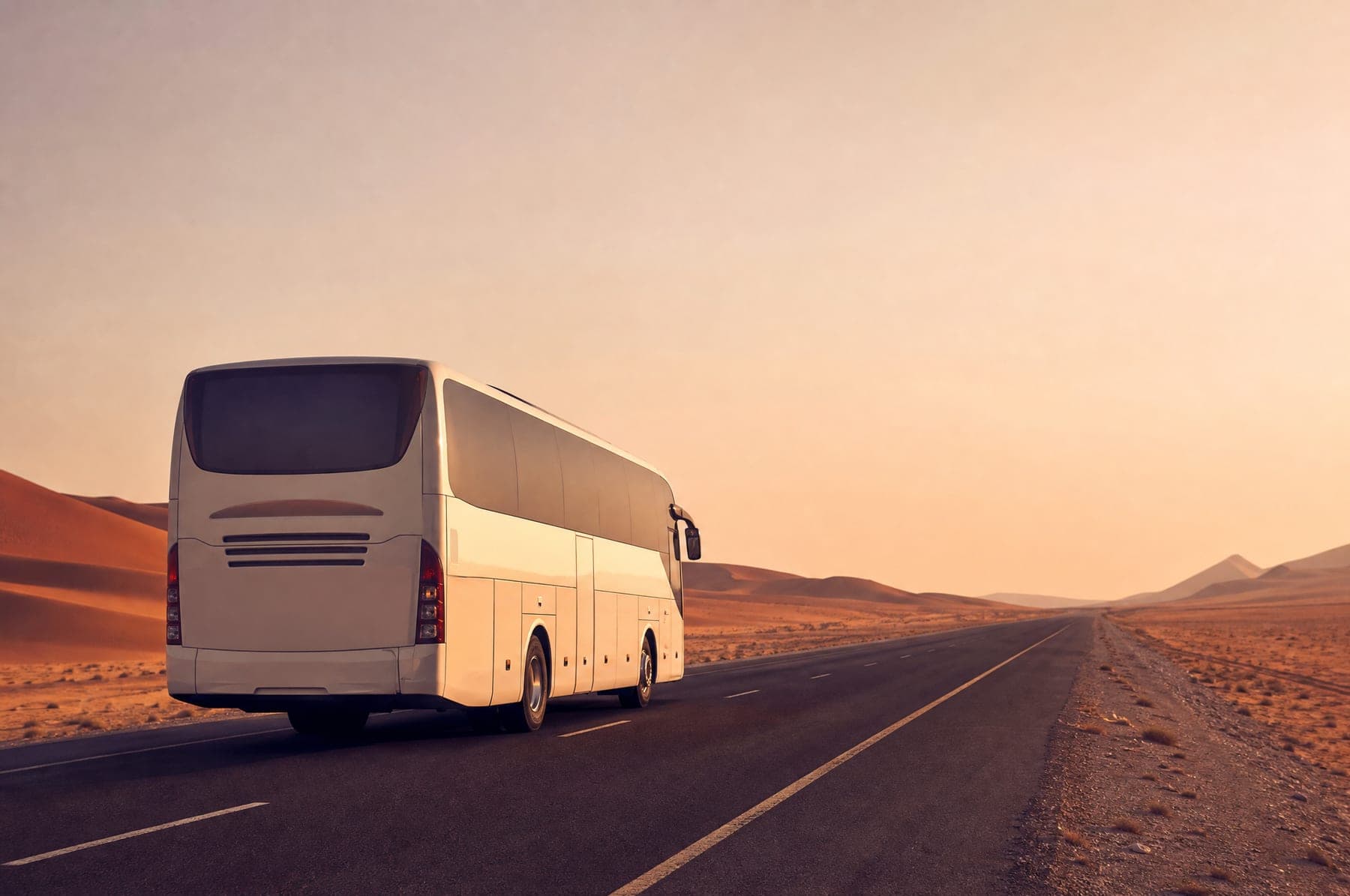 A modern white coach on a quiet desert highway at golden hour