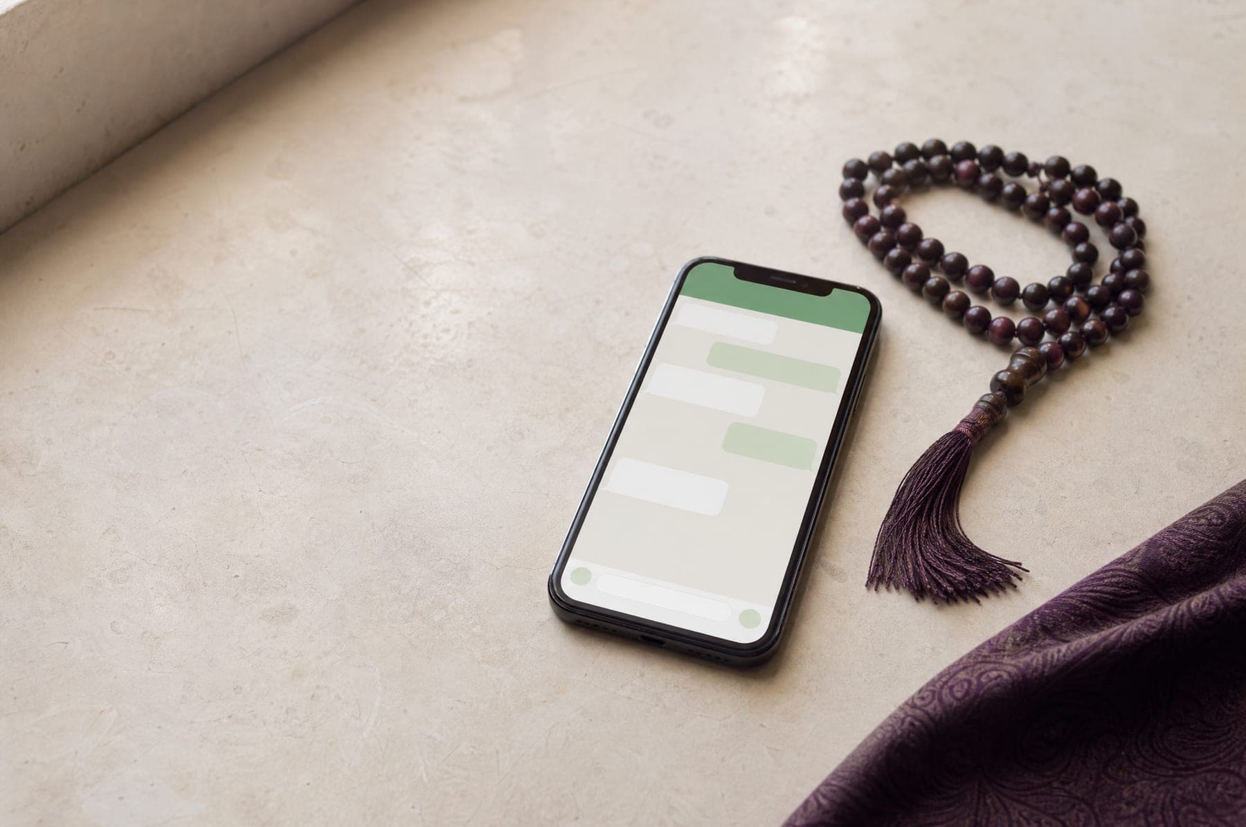 A phone showing a messaging app beside a string of prayer beads