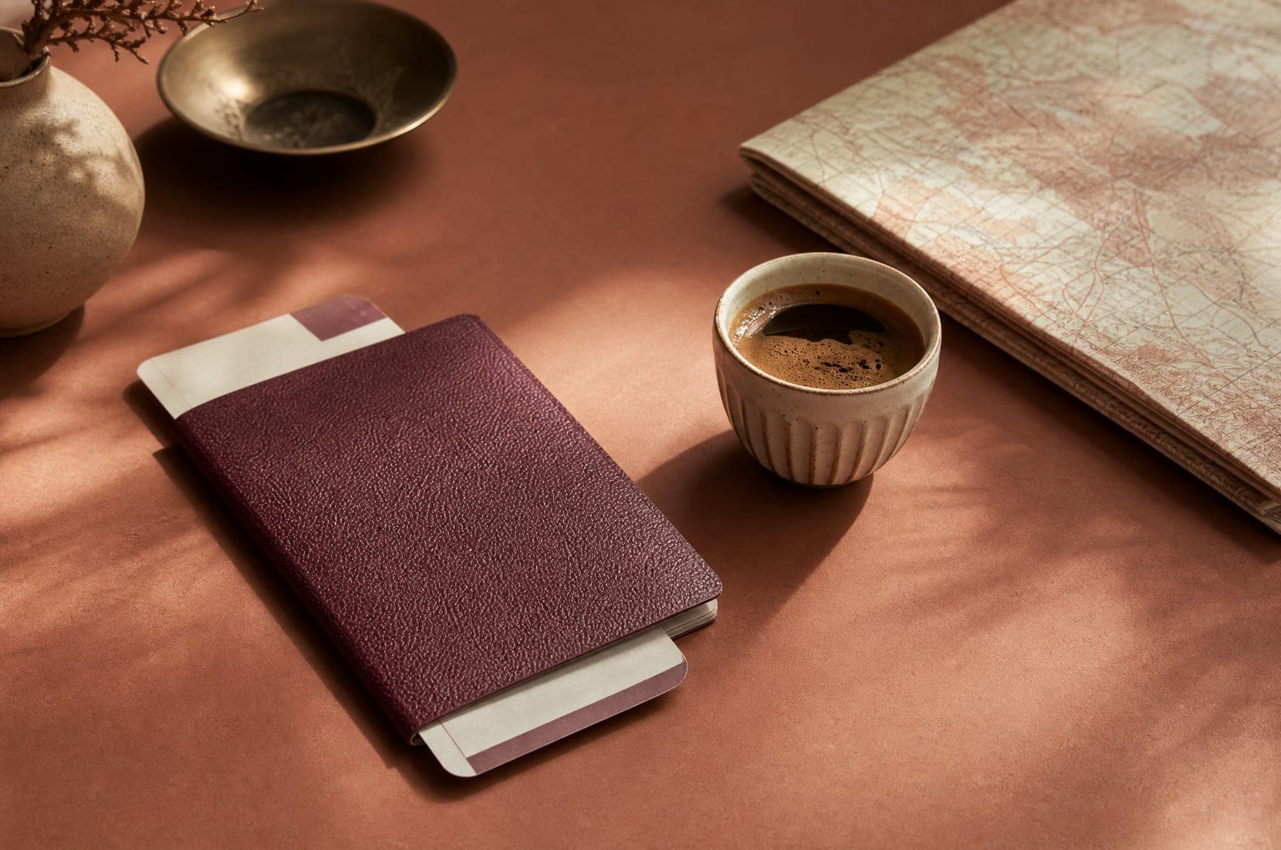 A passport with a boarding pass, a cup of coffee and a folded map on a desk